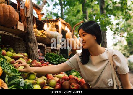 Donna in un mercato agricolo con frutta e verdura biologica. Donna asiatica in un mercato locale all'aperto. Foto Stock