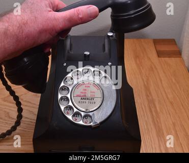 La mano di un uomo tiene la cornetta di un vecchio telefono o di un telefono a composizione rotante nero d'epoca, utilizzato in passato per effettuare chiamate telefoniche Foto Stock