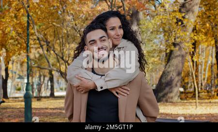 Felice etnico multirazziale ispanico sposato coppia all'aperto coccole su data in autunno parco sorridente partner ragazza abbracciante ragazzo da spalle uomo tenuta Foto Stock