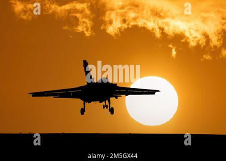 Caccia jet atterrando al tramonto con il cielo arancione e il grande sole al tramonto dopo una missione di combattimento. Tornado Fighter Bomber Foto Stock