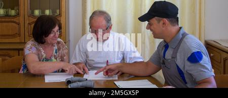 Immagine di un tecnico idraulico che porta una fattura per il lavoro da svolgere a una coppia anziana. Firma e stipula del contratto di lavoro. Foto Stock