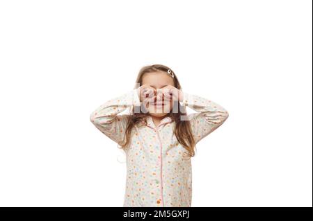 Adorabile bambina caucasica in pigiama, strofinando gli occhi al risveglio, isolata su sfondo bianco. Spazio di copia Foto Stock