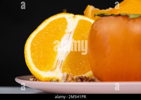 Mezzo arancione e un persimmon su un piatto su sfondo nero, spazio copia Foto Stock