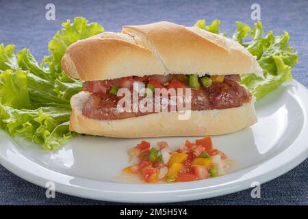 Choripan, tipico panino argentino con chorizo e salsa creola su un piatto. Foto Stock