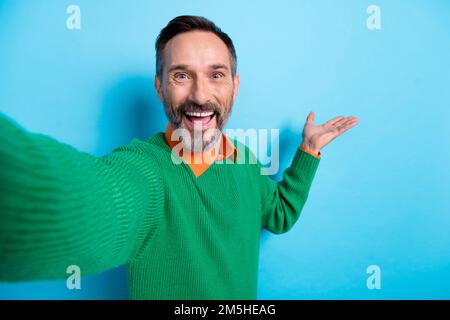 Foto ritratto di maturo bel mister streaming video Palm hold spazio vuoto vestito elegante verde vestiti isolati su sfondo di colore blu Foto Stock