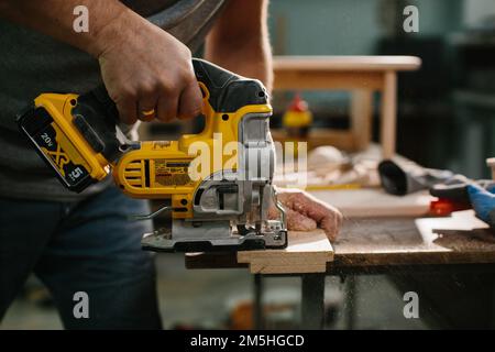 Primo piano a disposizione di falegname sconosciuto che lavora con un seghetto alternativo elettrico che taglia legno con la sega. Foto Stock