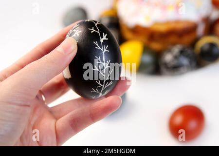 Sfocare l'uovo nero di Pasqua con ornamento dell'albero. Croffin torta di Pasqua. Primo piano uova di Pasqua pastello colorato su sfondo bianco. Festa di Pasqua minima Foto Stock
