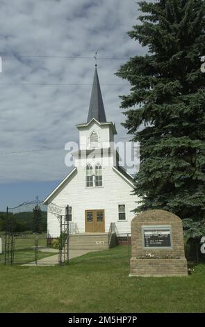 Sheyenne River Valley Scenic Byway - Waldheim Church e Entrance Arch. Il campanile bianco della Chiesa di Waldheim si innalza verso il cielo. Un arco di ferro nero sopra il marciapiede alle porte anteriori dice 'Waldheim Luth. Chiesa.' Location: Italy (46,667° N 97,934° W) Foto Stock