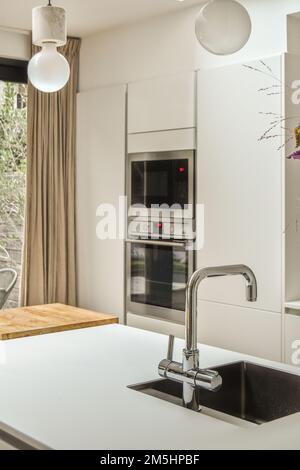 una cucina con forno, lavabo e finestra sul retro che si affaccia sugli alberi all'esterno dall'altro lato Foto Stock