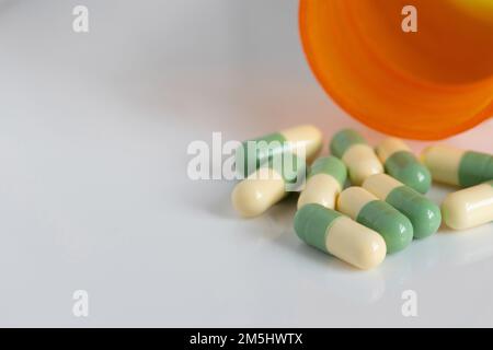 capsule pillole verdi e gialle con una bottiglia di farmaco di prescrizione versato su uno sfondo bianco con spazio di copia Foto Stock