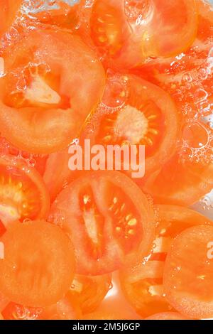 Primo piano fette fresche di pomodoro su sfondo bianco. Fette di pomodoro in acqua frizzante su fondo bianco, primo piano. Immagine verticale. Foto Stock
