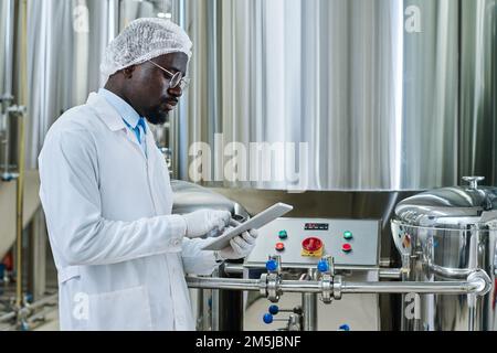 Ingegnere professionista in camice bianco davanti alle apparecchiature e che lavora online su un tablet pc Foto Stock