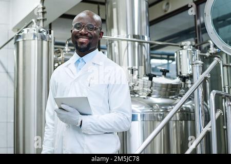 Ritratto di ingegnere afroamericano in cappotto bianco sorridente alla macchina fotografica che lavora in fabbrica Foto Stock