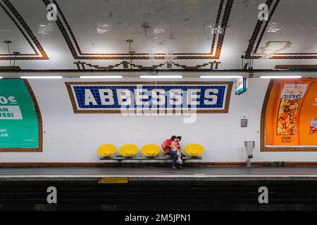 Parigi, Francia - la madre si siede sulla sedia gialla, coccola la figlia in grembo. Entrambi aspettano il prossimo treno all'interno della stazione della metropolitana Abbesses a Montmartre. Foto Stock