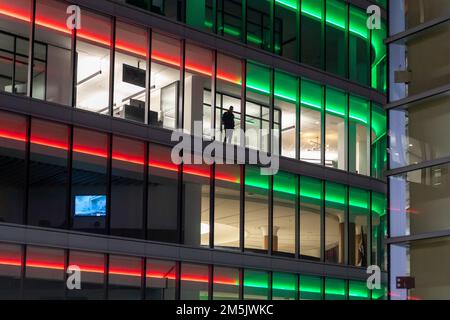 Detroit, Michigan - Un uomo guarda da una finestra nell'edificio degli uffici One Campus Martius decorato con luci rosse e verdi per l'inverno Foto Stock