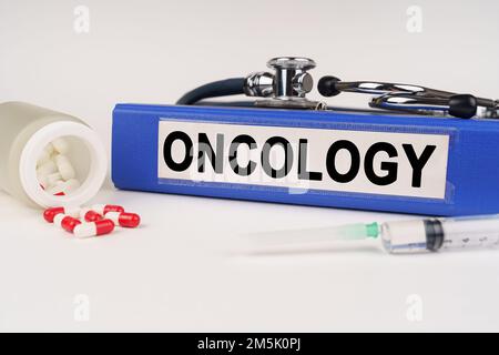 Concetto medico. Su una superficie bianca ci sono pillole, una siringa, uno stetoscopio e una cartella con l'iscrizione - Oncologia Foto Stock