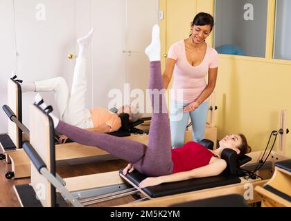 Ispano femmina pilates istruttore aiutando ragazza esercitandosi sul reformer Foto Stock