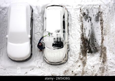 Autista che pulisce la neve dalla macchina su un parcheggio, vista dall'alto. Nevicate nella città d'inverno Foto Stock