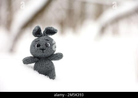 Coniglio lavorato a maglia grigio in una neve su sfondo di foresta sfocata, biglietto d'auguri. Simbolo del Capodanno cinese 2023 Foto Stock