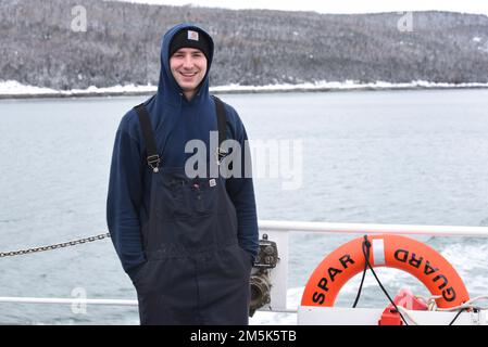 STATI UNITI Coast Guard Petty Officer 3rd Class Michael Covey, un tecnico di macchinari a bordo di Cost Guard Cutter Spar, posa per una foto sul fantastico mentre si è in corso nella St. Lawrence River, 21 marzo 2022. Spar e il suo equipaggio si recano a Duluth, Minn. Dopo un periodo di manutenzione di un anno a Baltimora. Foto Stock