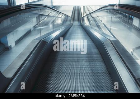 Messa a fuoco selettiva in primo piano con una lunga rampa mobile discendente vuota, con un pavimento in scala di grigi striato che si muove continuamente su un nastro di circolazione Foto Stock