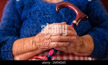 Primo piano della nonna che tiene un bastone da passeggio mentre si siede sul divano nel soggiorno. Donna di 90s anni sul divano a casa. Concetto di persone anziane. Foto Stock