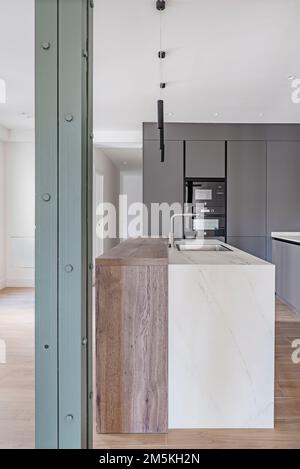 Una moderna cucina recentemente arredata con una parte di legno, parte di marmo chiaro con un lavandino costruito e una colonna di metallo dipinta di verde Foto Stock