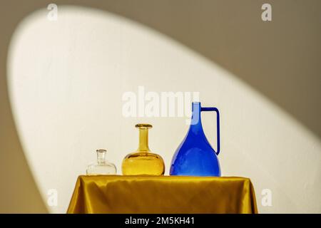 Vasi decorativi in vetro di colori diversi su una struttura in tessuto dorato sotto la luce di un riflettore Foto Stock