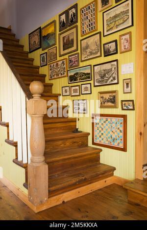 Parete con scala decorata con cornici a quadri nella sala da pranzo all'interno di una casa in legno in stile cottage di campagna. Foto Stock