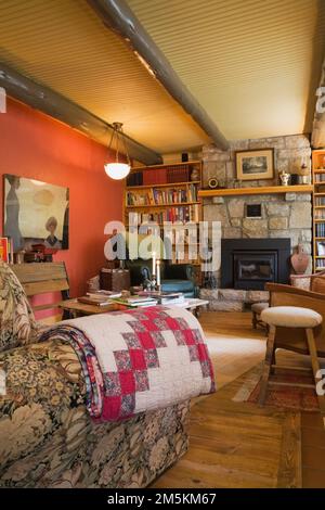 Caminetto in pietra tagliata delimitato da librerie e vecchi mobili e arredi nel soggiorno all'interno di un cottage di campagna in legno di casa. Foto Stock