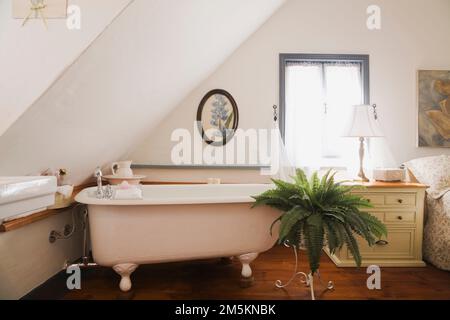La vasca da bagno bianca con letto pieghevole e il tavolo terminale sono collegati al letto nella camera da letto principale al piano superiore, all'interno di una casa in legno ricostruita degli anni '1840. Foto Stock