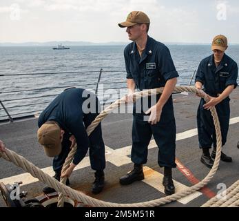 OKINAWA, Giappone (24 marzo 2022) i marinai passano una linea sotto il ponte a bordo del cacciatorpediniere missilistico guidato di classe Arleigh Burke USS Ralph Johnson (DDG 114). Ralph Johnson è assegnato alla Task Force 71/Destroyer Squadron (DESRON) 15, la più grande DESRON della Marina e la principale forza di superficie della flotta statunitense 7th. Foto Stock