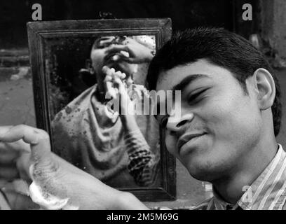 Un barbiere rasa un uomo a Kolkata , India. Foto Stock