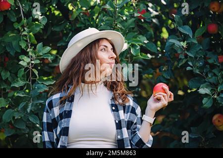 Donna in un cappello che tiene la mela rossa matura dall'albero. Raccolto autunnale Foto Stock