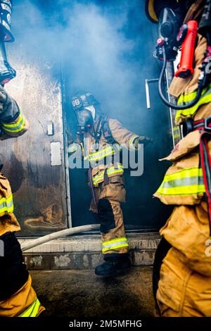 Un vigile del fuoco con installazioni del corpo Marino Pacific Fire and Emergency Services esce da una sala di combustione durante un esercizio bilaterale di addestramento al fuoco vivo a Camp Hansen, Okinawa, Giappone, 25 marzo 2022. MCIPAC F&ES e il Vigili del fuoco di Naha hanno assemblato e condotto corsi di formazione in tempo reale per confrontare le diverse tecniche e metodi antincendio utilizzati da ciascun reparto per svolgere la stessa missione. Foto Stock