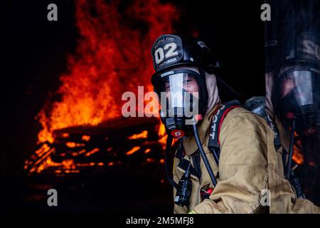 Un vigile del fuoco con installazioni del corpo Marino Pacific Fire and Emergency Services osserva una sala di combustione durante un esercizio bilaterale di addestramento al fuoco vivo a Camp Hansen, Okinawa, Giappone, 25 marzo 2022. MCIPAC F&ES e il Vigili del fuoco di Naha hanno assemblato e condotto corsi di formazione in tempo reale per confrontare le diverse tecniche e metodi antincendio utilizzati da ciascun reparto per svolgere la stessa missione. Foto Stock
