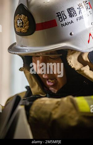 Un vigile del fuoco con il Vigili del fuoco di Naha stabilisce la comunicazione radio mentre risponde ad un incendio durante un esercizio bilaterale di addestramento al fuoco vivo a Camp Hansen, Okinawa, Giappone, 25 marzo 2022. Installazioni di corpi marini Pacific Fire and Emergency Services e il Dipartimento dei vigili del fuoco di Naha City hanno riunito e condotto corsi di formazione dal vivo per confrontare le diverse tecniche e metodi antincendio utilizzati da ciascun reparto per realizzare la stessa missione. Foto Stock