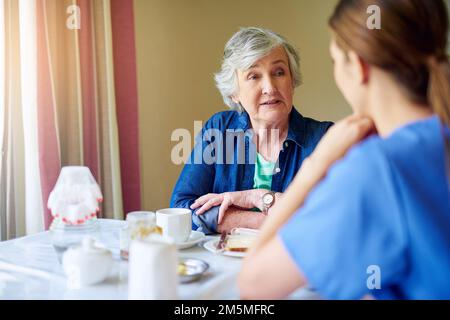 Chiacchierare un po' con la colazione. un residente e un'infermiera in una casa di riposo. Foto Stock