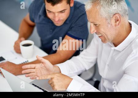 HES ha avuto un'idea e theyre che funziona con esso. Scatto ad angolo alto di due uomini che lavorano in ufficio. Foto Stock