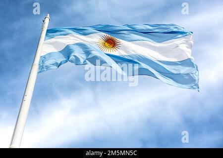 La bandiera argentina sventola su un palo di metallo bianco sotto il cielo nuvoloso blu in una giornata di sole Foto Stock