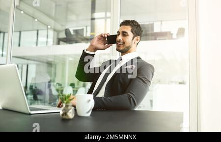 Fa sentire tutti i suoi clienti come VIP. un uomo d'affari che parla sul suo cellulare mentre guarda il suo portatile. Foto Stock