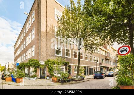 una strada con auto parcheggiate di fronte a edifici e alberi su entrambi i lati della strada è un segno che dice che non parcheggio Foto Stock