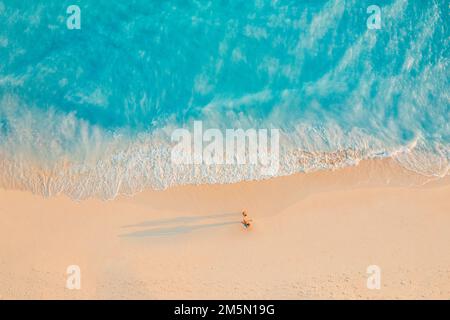 Vista aerea di una splendida spiaggia con una coppia che cammina al tramonto vicino al mare turchese. Vista dall'alto del paesaggio estivo della spiaggia, romantica ispirazione Foto Stock