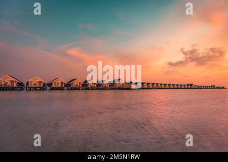 Tramonto sull'isola delle Maldive, resort di lusso con ville sull'acqua e molo in legno. Cielo e nuvole mozzafiato e sfondo spiaggia per le vacanze estive Foto Stock