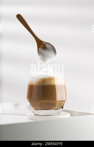 Utilizzare un cucchiaio di legno per versare la schiuma di latte in una tazza di cappuccino. Foto Stock