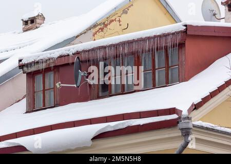 Ghiaccioli e neve sul tetto della casa in una giornata invernale innevata tra il disgelo. Pulizia del tetto da neve e ghiaccio. Foto Stock