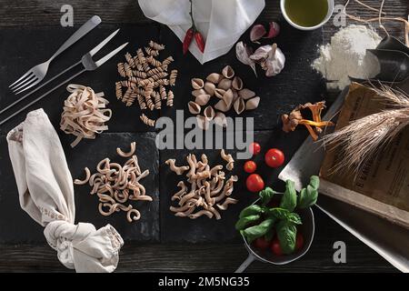 Elegante immagine della pasta italiana con pomodori ciliegini, basilico, grano e farina su sfondo nero Foto Stock