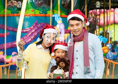 Felice tre indossando un cappello di Natale nel parco divertimenti per giocare Foto Stock