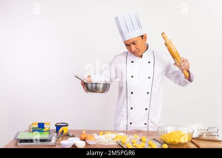 chef maschio arrabbiato che tiene una ciotola di pasta e di rolling pin Foto Stock