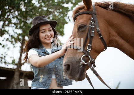 bella ragazza cowboy asiatica in piedi accanto a cavallo su sfondo all'aperto Foto Stock